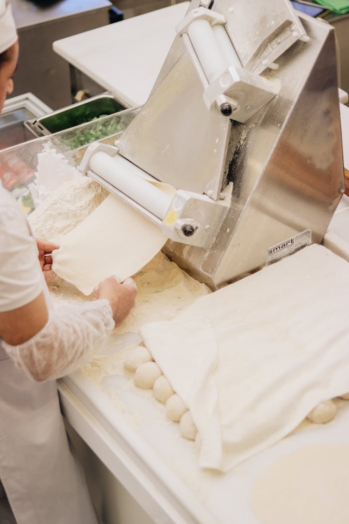 Woman operating dough machine in factory setting, showcasing bread preparation.